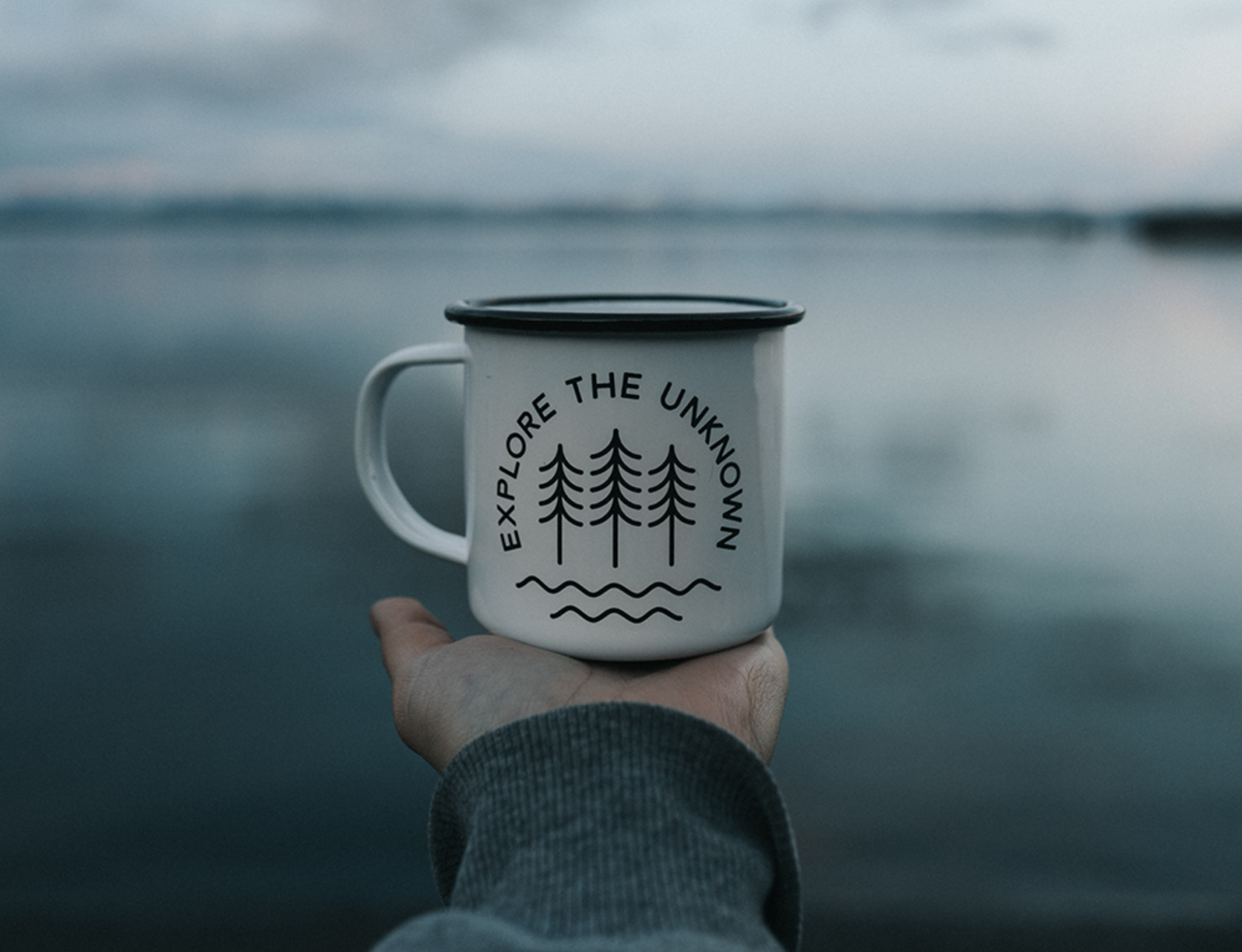 Person holding a coffee mug with the words explore the unknown